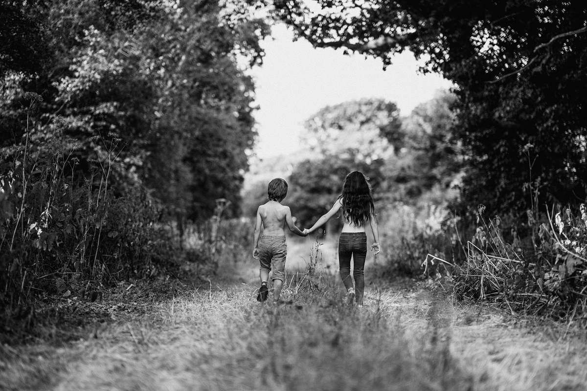 holding hands grayscale photo of boy and girl walking on path hand